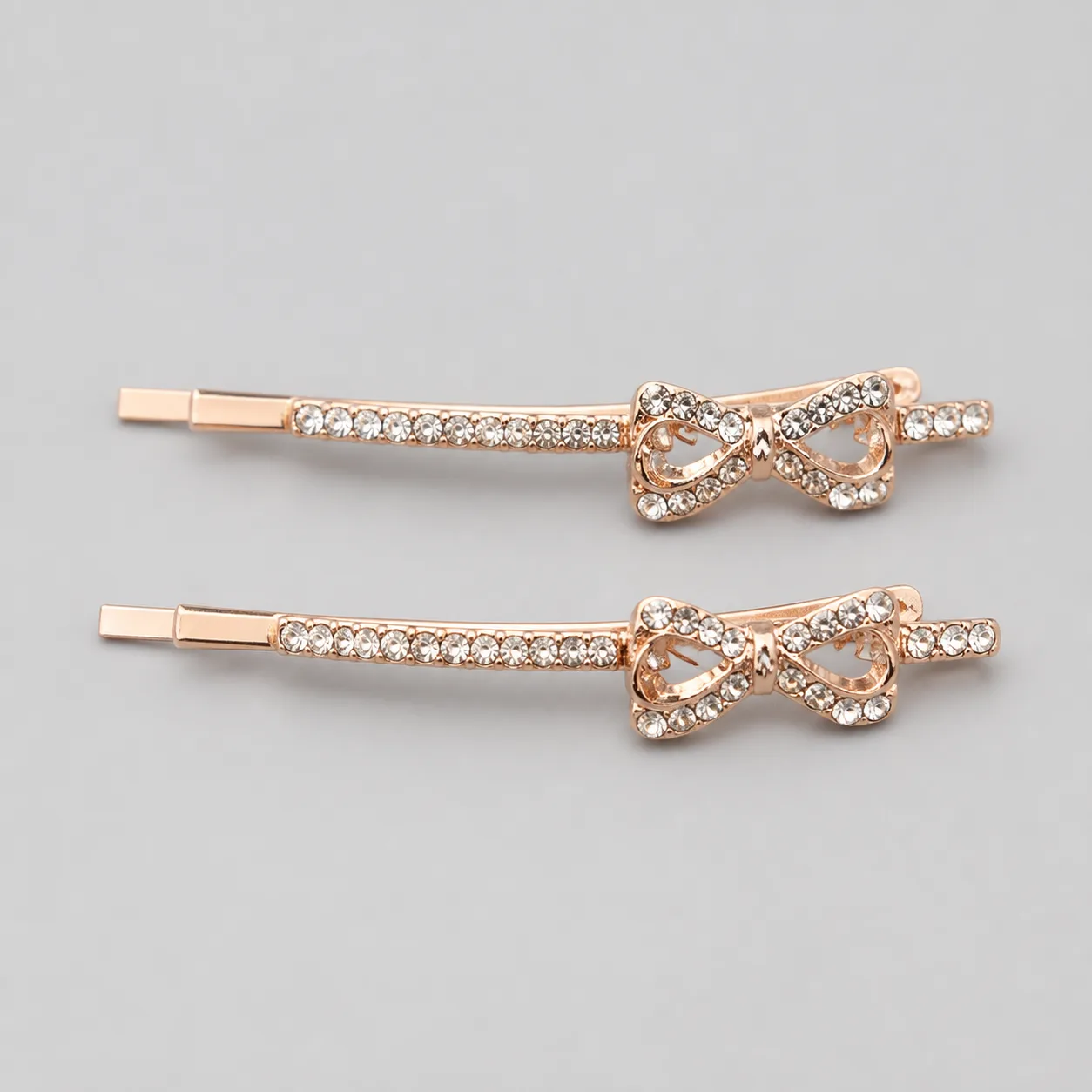 Conjunto de 2 Ganchos Rosa Dourado com Laço de Cristais Par de ganchos com laço de cristais sobre fundo pérola