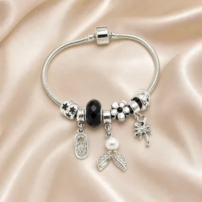 Pulseira prateada com berloques pretos, uma pulseira sobre cetim bege