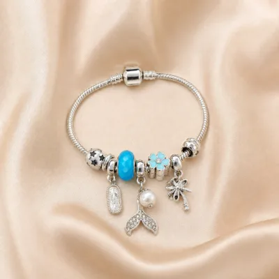 Pulseira prateada com berloques azuis, uma pulseira sobre cetim bege