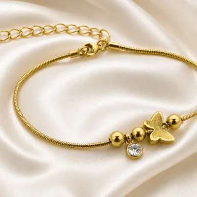 pulseira dourada com borboleta, contas e cristal em cetim marfim, referência 85383-4