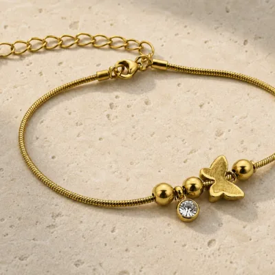 pulseira dourada com borboleta, contas e cristal em pedra clara de tom quente, referência 85383-4