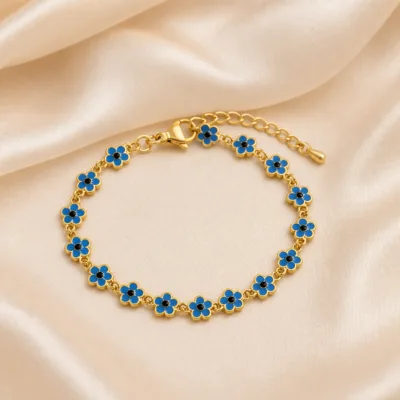 Pulseira dourada de flores azuis com centros pretos, uma pulseira, sobre cetim bege