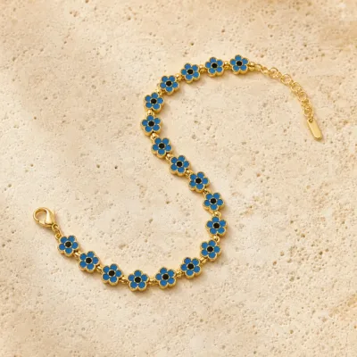 Pulseira dourada de flores azuis com centros pretos, uma pulseira, sobre pedra quente