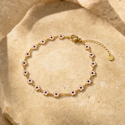 Pulseira dourada de flores rosa com centros pretos, uma pulseira, sobre pedra quente