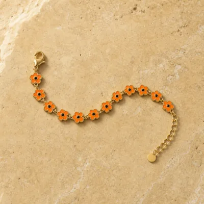 Pulseira dourada de flores laranja com centros pretos, uma pulseira, sobre pedra quente