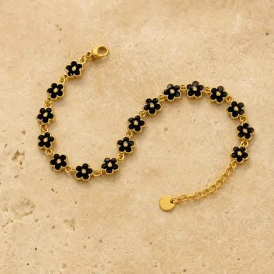 Pulseira dourada de flores pretas, uma pulseira, sobre pedra quente