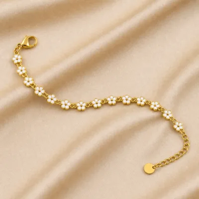 Pulseira dourada de flores brancas, uma pulseira sobre cetim bege