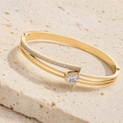 bracelete triplo com barra de cristais e gota, variante dourada, pedra clara, referência 85580-4