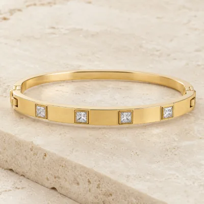 Pulseira dourada rígida com quatro cristais quadrados sobre pedra quente