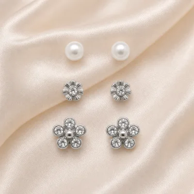 Conjunto de 3 pares de brincos prateados florais sobre cetim bege claro