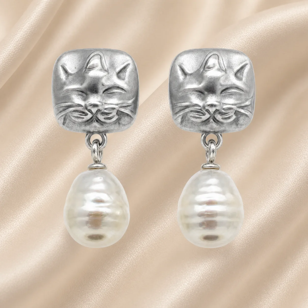 Brincos prateados de gato com pérolas sobre cetim bege claro