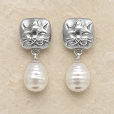 Brincos prateados de gato com pérolas sobre pedra de tom quente