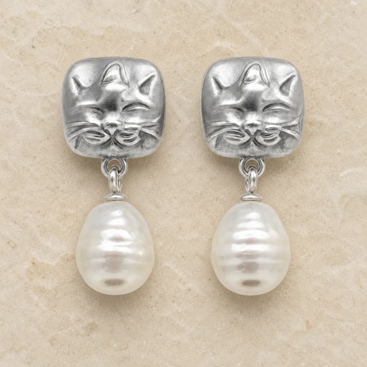 Brincos prateados de gato com pérolas sobre pedra de tom quente