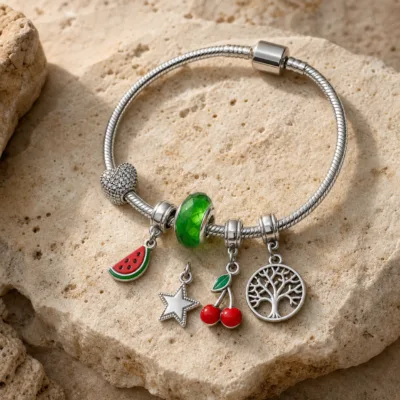 Pulseira Prateada de Aço com Berloques de Cereja Verde sobre pedra quente