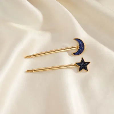 Conjunto de ganchos dourados com lua e estrela sobre cetim