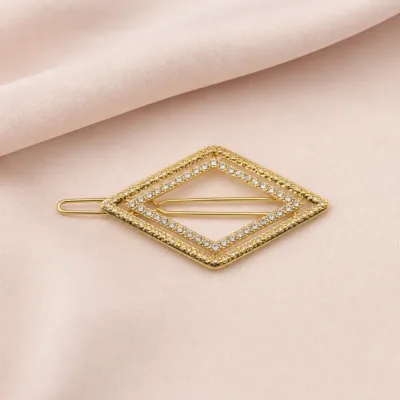 Gancho de cabelo dourado com cristais sobre tecido bege rosado