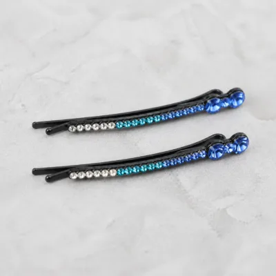 Dois ganchos pretos com strass em degradé azul sobre pedra clara