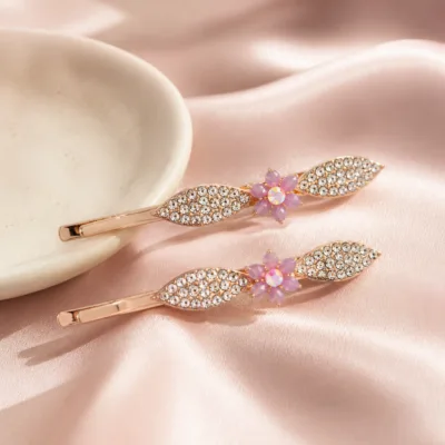 Dois ganchos ouro rosa com flor lilás sobre cetim rosa