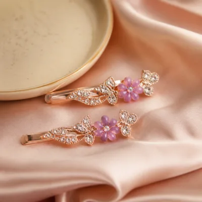 Dois ganchos ouro rosa com borboletas e flor lilás sobre cetim