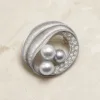 Broche oval prateado com três pérolas cinzentas e cristais