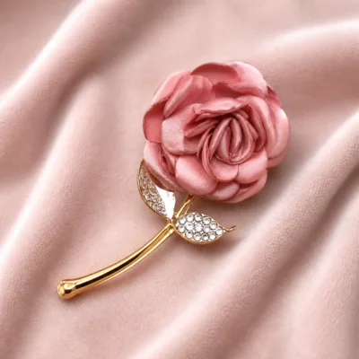 Broche floral rosa com haste dourada sobre tecido acetinado