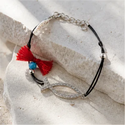 Pulseira preta com peixe prateado e cristais sobre pedra clara