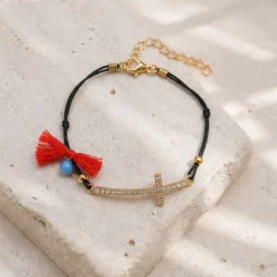 Pulseira preta com cruz dourada e cristais sobre pedra clara