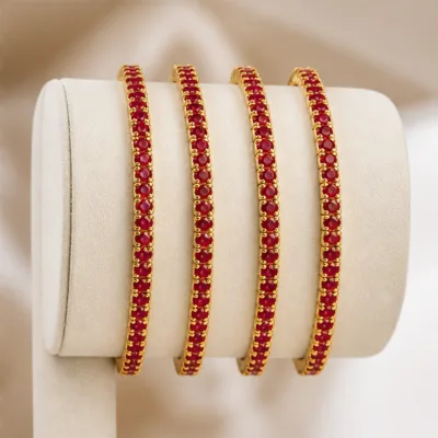 Quatro pulseiras douradas com cristais vermelhos num expositor