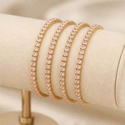 Quatro pulseiras douradas com cristais rosa-claro num expositor