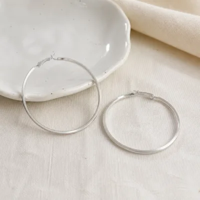 Par de argolas prateadas de 60 mm numa composição de tons neutros