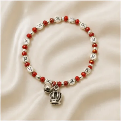 Pulseira vermelha com contas OK e coroa sobre tecido claro