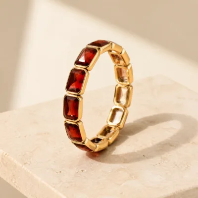 Pulseira dourada de vidro vermelho sobre pedestal claro