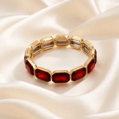 Pulseira dourada com vidro vermelho sobre cetim marfim