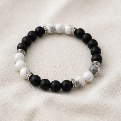 Pulseira de pedra natural preta e branca sobre tecido neutro