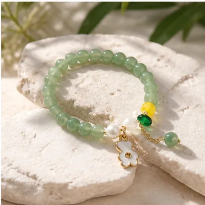 Pulseira verde de contas com flor dourada sobre pedra clara