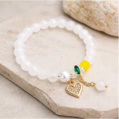 Pulseira branca de contas com coração de cristais sobre pedra clara