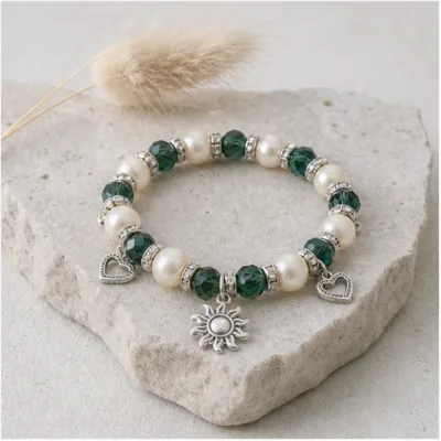 Pulseira vermelha de pérolas e cristais com sol prateado sobre pedra clara