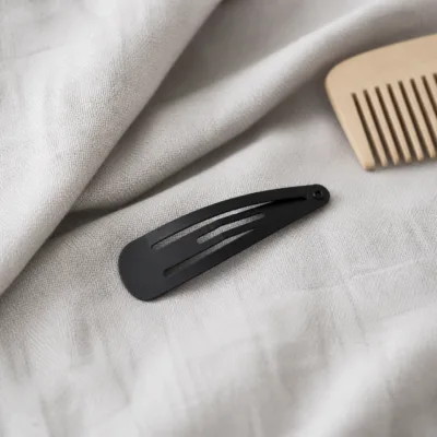 Gancho de cabelo preto alongado sobre tecido cinzento-claro