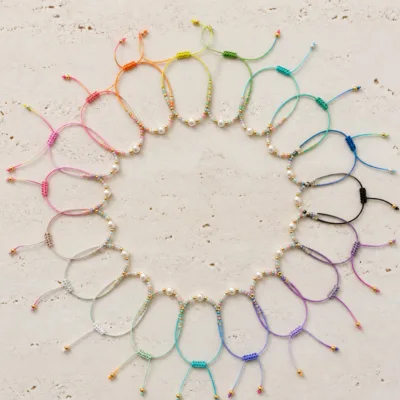 Pulseiras ajustáveis coloridas com pérola central numa composição plana