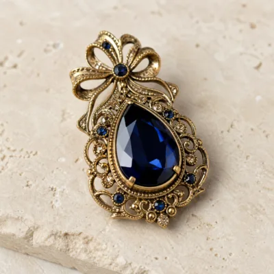 Alfinete gota dourado com cristal azul-escuro em detalhe