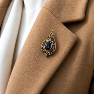 Alfinete gota dourado com cristal azul aplicado num casaco camel