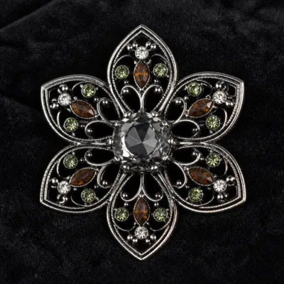 Alfinete flor prateado com cristais verdes e âmbar em detalhe