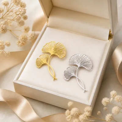 Alfinetes de ginkgo dourado e prateado numa caixa de joalharia