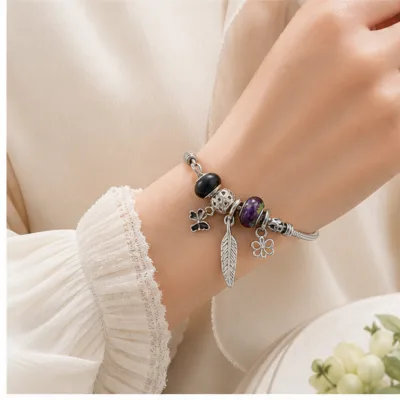 Pulseira de charms preta e roxa com pena usada no pulso