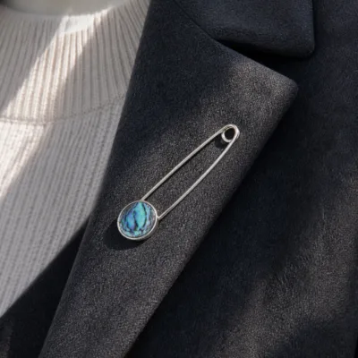 Alfinete de segurança prateado com madrepérola aplicado num blazer cinzento
