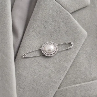Alfinete prateado com pérola oval aplicado num blazer cinzento