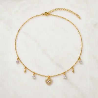 Colar dourado delicado com pendente e cristais sobre fundo claro