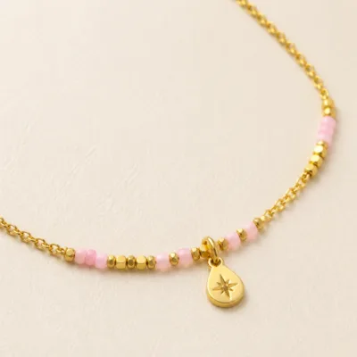 Pormenor das missangas rosa-claro e do pendente dourado