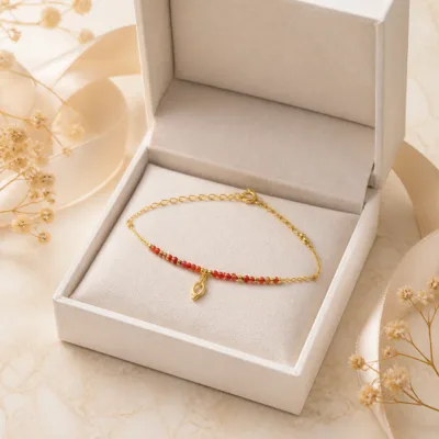 Pulseira dourada com missangas vermelhas e pendente em caixa de joalharia