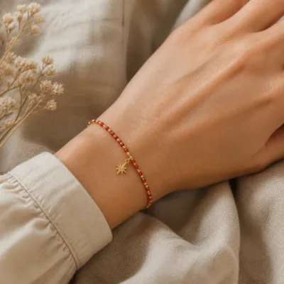 Pulseira dourada com missangas vermelhas e pendente apresentada no pulso